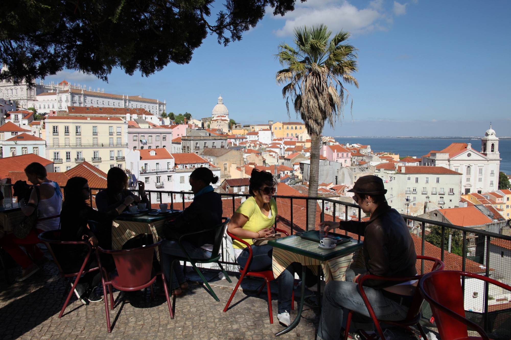 This April 9, 2011 photos shows tourists as they sit in the shade at an outdoor cafe overlooking Lisbon's Alfama old quarter along the Tagus river in Portugal. Portugal is immersed in debt and is widely expected to receive a Greek-style bailout by June. But travelers willing to jump aboard this economic rollercoaster could find bargains in a country small enough to tour in a week's time. (AP Photo/Armando Franca)
