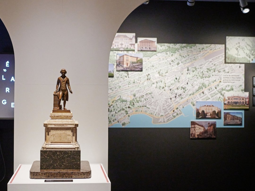 Au premier plan, une réplique du monument de Pury. A l'arrière plan à droite, un plan de Neuchâtel présentant des demeures "édifiées grâce au commerce international".