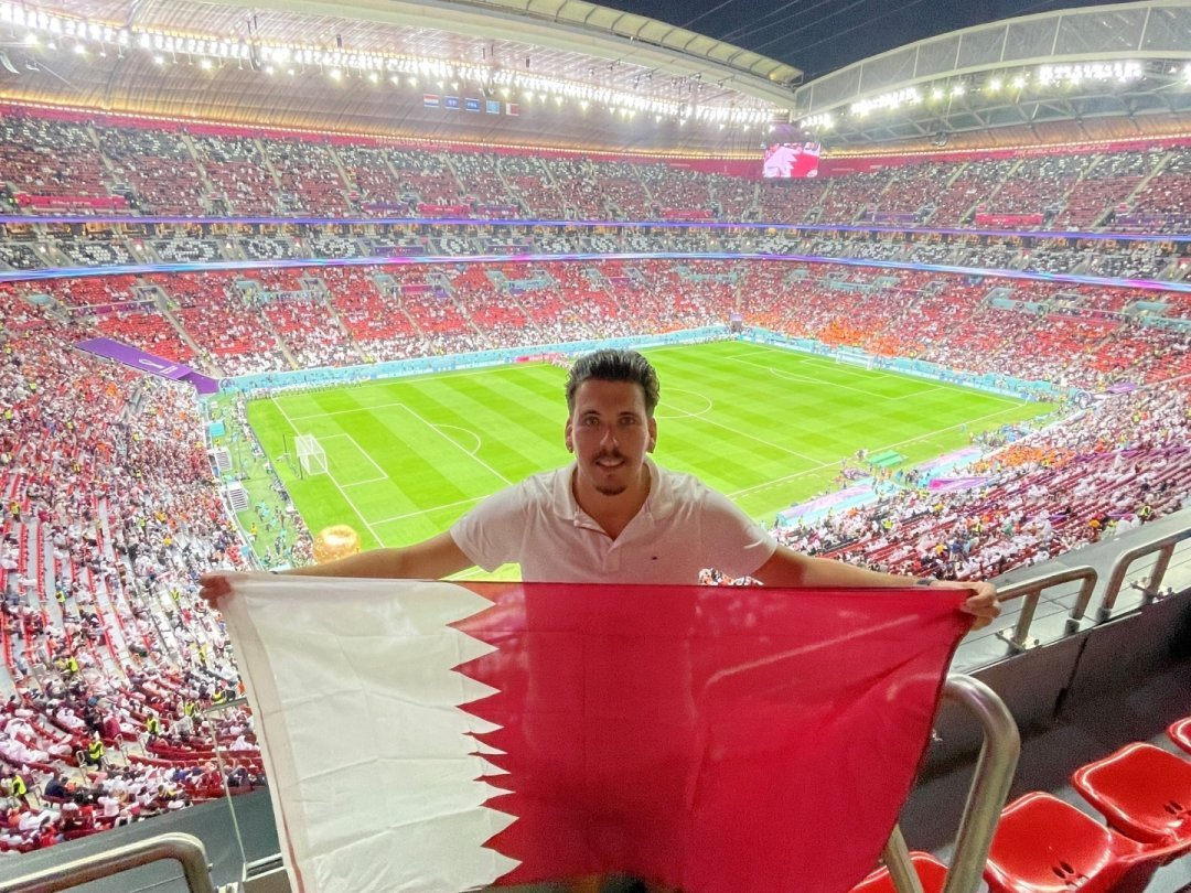 Kevin Gomes prend la pose avec un drapeau du Qatar au Al Bayt Stadium.