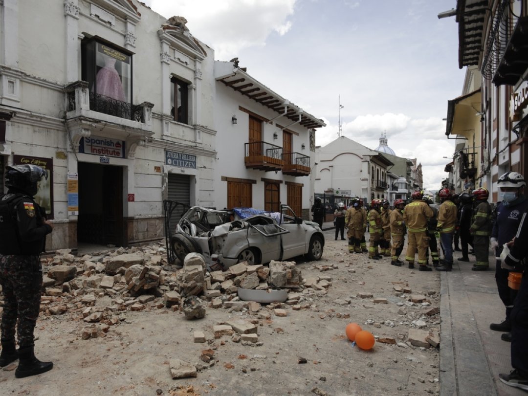 Des secouristes se tiennent à côté d'une voiture écrasée par des débris après un tremblement de terre à Cuenca, en Équateur.