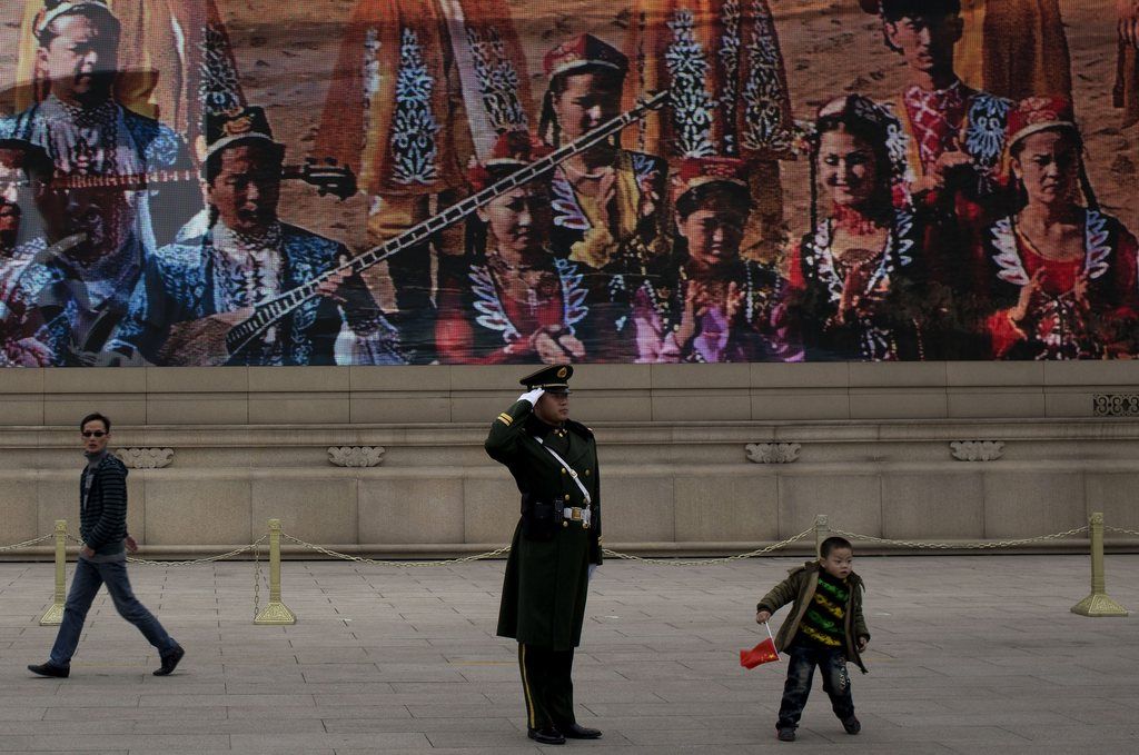 A child holds a Chinese national flag as he runs past a paramilitary policeman in front of a display depicting Xinjiang people on Tiananmen Square during the 205-member Central Committee's third annual plenum in Beijing Saturday, Nov. 9, 2013. Reform advocates are looking to China's leaders to launch a new era of change by giving entrepreneurs a bigger role in the state-dominated economy and farmers more control over land at a policymaking conference that opened Saturday. (AP Photo/Andy Wong)
