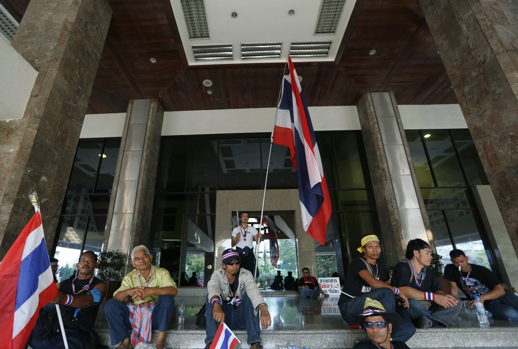 epa03964680 Thai anti-government protesters sit outside the building after they stormed into the Public Relations Department in Bangkok, Thailand, 25 November 2013. Thousands of protesters occupied parts of the Finance Ministry in an effort to paralyze the government of Thai Prime Minister Yingluck Shinawatra. The protesters, blowing whistles and carrying flowers, marched on 13 government offices including state-owned television stations, military and police headquarters, the parliament and Government House where the cabinet meets to overthrow the 'Thaksin regime.'  EPA/NARONG SANGNAK