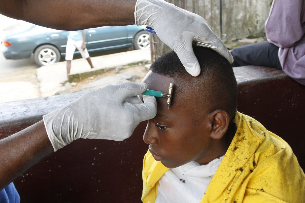 epa04396862 A Liberian barber shaves the head of a client wearing latex gloves as a preventive measure against the deadly Ebola virus in Monrovia, Liberia 12 September 2014. The World Health Organization (WHO) has said the number of deaths from Ebola has risen to 2100 in West Africa with an exponential surge predicted in Liberia the hardest hit country in the region.  EPA/AHMED JALLANZO
