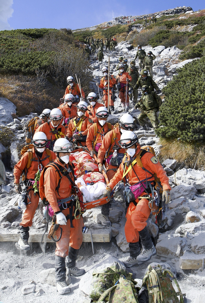 In this Sunday, Sept. 28, 2014 photo released by Tokyo Fire Department, firefighters carry an injured by Saturday's initial eruption from the summit of Mount Ontake in central Japan. A dozen more bodies were found Wednesday, Oct. 1 near the ash-covered summit of the Japanese volcano as searches resumed amid concern of toxic gasses and another eruption. (AP Photo/Tokyo Fire Department) EDITORIAL USE ONLY