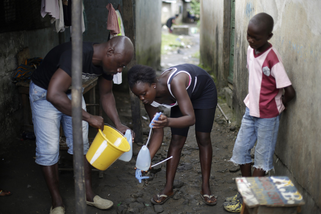 In this photo taken Thursday Oct. 2, 2014, Promise Cooper, 16,  is helped filling a bottle with  chlorine solution by  Kanyean Molton Farley, a community activist who visits Promise and her two brothers, Emmanuel Junior, 11, right,  and Benson, 15, not pictured,  on a daily basis at their St. Paul Bridge home in Monrovia, Liberia. The Cooper children are now orphans, having lost their mother, Princess, in July, and their father Emmanuel in August. Their 5-month-old baby brother Success also succumbed to the virus in August. Ruth, their 13-year-old sister is being hospitalized with Ebola. The three never fell sick to the deadly disease. (AP Photo/Jerome Delay)
