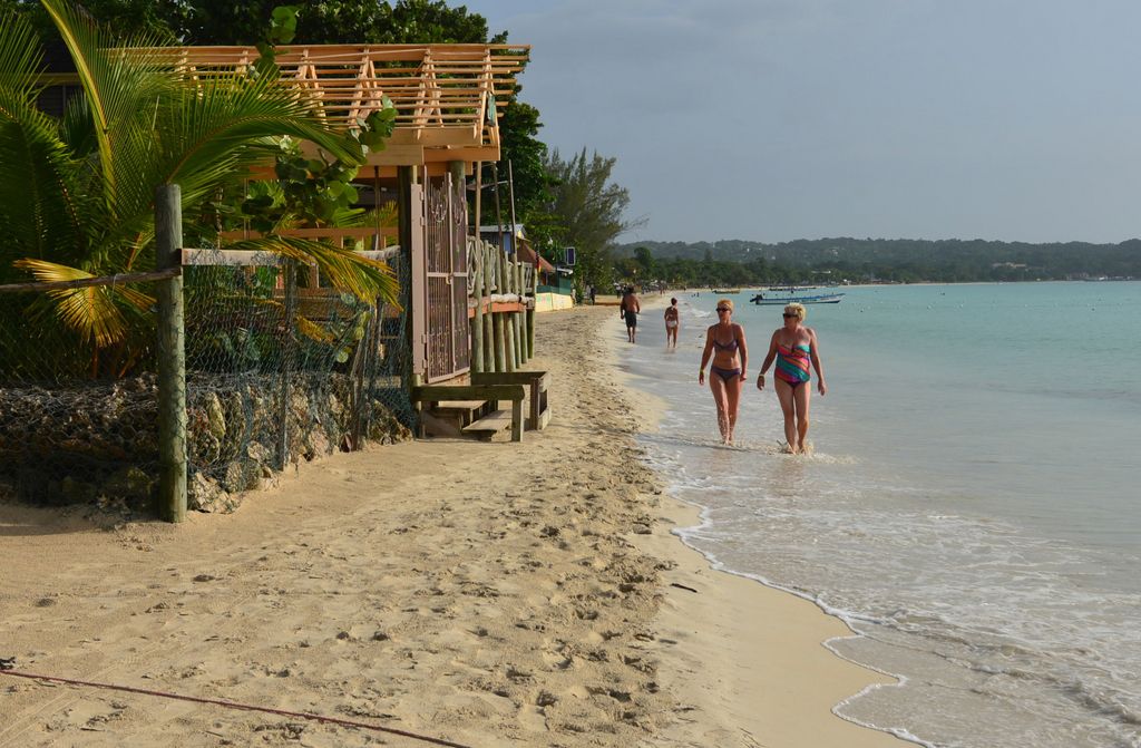 In this Sept. 14, 2014 photo, sunbathers walk along a badly eroding patch of resort-lined crescent beach in Negril in western Jamaica. Some sections of the beach are barely wide enough for a decent-sized beach towel and the Jamaican National Environment and Planning Agency says the sands are receding at a rate of more than a meter (a yard) per year. (AP Photo/David McFadden)
