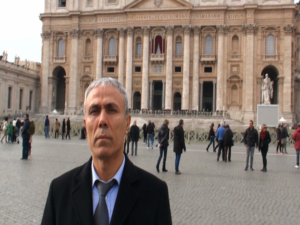 In this image taken from a video provided by Adnkronos International, Ali Agca stands in front of St. Peter's Basilica at the Vatican, Saturday, Dec. 27, 2014. The Turkish gunman who shot and wounded John Paul II in 1981 laid white flowers Saturday on the saint's tomb in St. Peter's Basilica, Vatican officials said. A Vatican spokesman, the Rev. Ciro Benedettini, said the surprise visit by Mehmet Ali Agca, believed to be his first time in the Vatican since the assassination attempt, lasted a few minutes. As with other flowers left by visitors to the tomb, the blossoms were later removed by basilica workers. (AP Photo/Adnkronos International, ho)