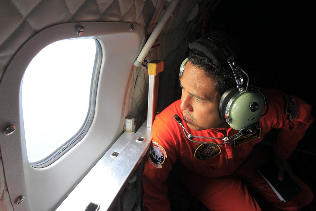 epa04542664 An Indonesia's Air Force crewman looks out of the window during a search and rescue operation as they search for the missing AirAsia plane in Indonesia, 30 December 2014. A search aircraft looking for the missing AirAsia plane spots objects on the ocean surface. Footage taken from the helicopter showed a triangular orange object and several smaller white objects, around 10 in total, but it was not clear what they were, Metro TV said. Ships and aircraft have been sent to the area to investigate further.  EPA/BAGUS INDAHONO