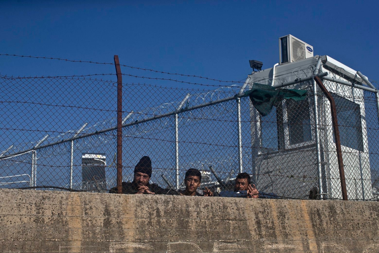 Three men stand by the fence of the migrant and refugee registration camp in Moria, on the island of Lesbos, Greece, Thursday, Nov. 5, 2015. The European Union predict that around 3 million more migrants are expected to arrive in the 28-nation bloc by the end of next year. (AP Photo/Marko Drobnjakovic) Greece Migrants