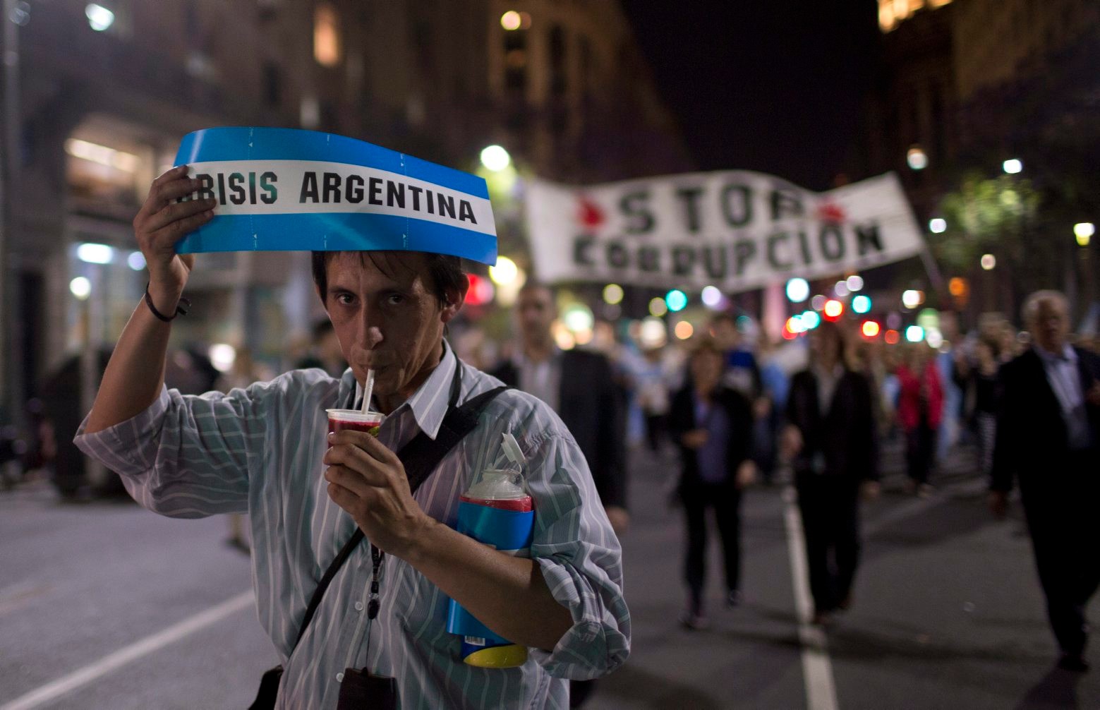A man holds a banner reading in Spanish "Argentina Crisis" as he drinks mate, a herbal tea, during a protest against the government of Argentina's President Cristina Fernandez in Plaza de Mayo in Buenos Aires, Argentina, Thursday, Nov. 13, 2014.  (AP Photo/Natacha Pisarenko) APTOPIX Argentina Protest