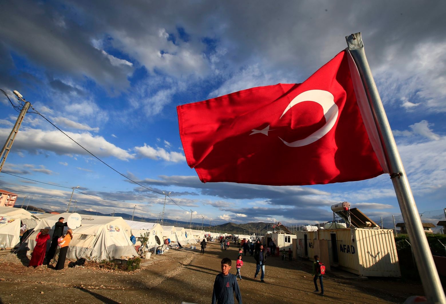 FILE - In this Wednesday, March 16, 2016 file photo a Turkish flag flies at the refugee camp for Syrian refugees in Islahiye, Gaziantep province, southeastern Turkey.  German Chancellor Angela Merkel and top European Union officials plan to travel close to Turkeyís border with Syria in hopes of promoting a troubled month-old agreement to manage a refugee crisis that has left hundreds of thousands stranded on the migrant trail to Europe. (AP Photo/Lefteris Pitarakis, File) Europe Migrants Turkey