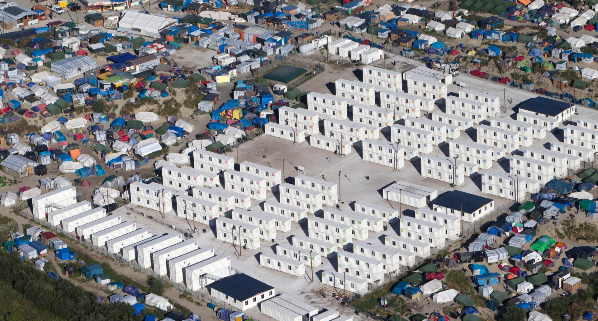 FILE - This Aug. 24, 2016 file photo shows an aerial view of the migrant camp in Calais, northern France. Tempers are rising among migrants squeezed in record numbers into a shrinking slum camp in France's port city of Calais, where hours-long waiting lines for food and showers and the tightening grip of security forces are leaving emotions raw. (AP Photo/Michel Spingler, File) France Migrants Tensions