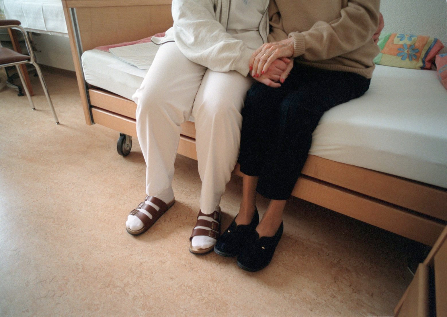 ARCHIV --- Eine Pflegerin haelt einer Bewohnerin im Pflegeheim Belvoir in Bern auf dem Bett sitzend die Haende, aufgenommen am 27. Januar 2004 . - In der Schweiz lebt nur ein verschwindend kleiner Anteil der 65- bis 79-Jaehrigen in Pflegeheimen, wie am Montag, 10. Dezember 2007 bekanntgegeben wurde. Die Aufenthaltsdauer in Pflegeheimen betraegt im Schnitt knapp 1.000 Tage. Ueber 85 Prozent des Personals sind Frauen, wie eine BFS-Statistik zeigt. (KEYSTONE/Gaetan Bally)   SCHWEIZ PFLEGEHEIM