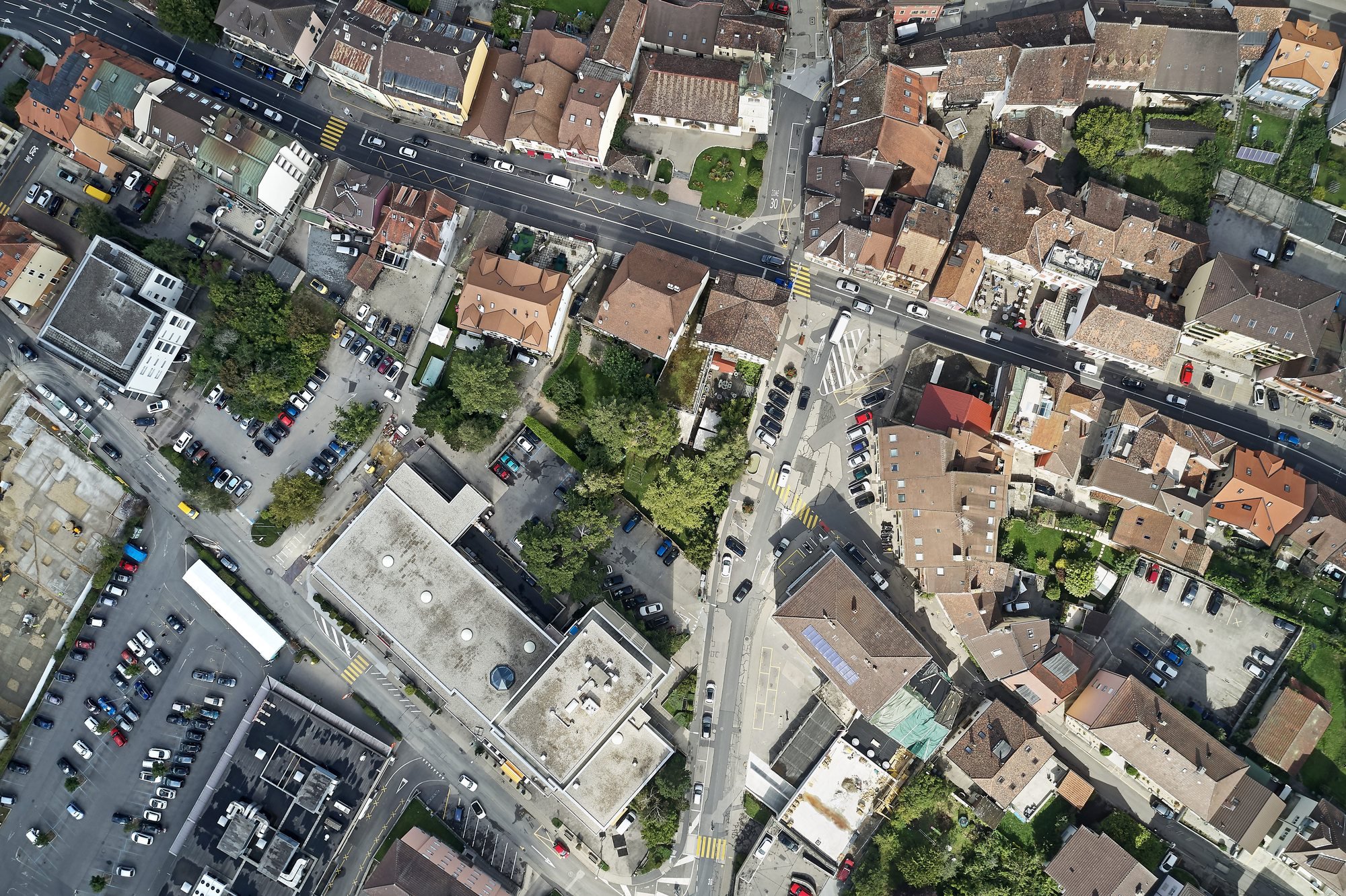 Vue aérienne de Peseux avec, au centre, la place de la Fontaine et au nord, la place du Temple, séparées par la H10. En bas à gauche, la Migros et ses places de parc bordent la rue Jämes-Paris et font face à Cap 2000.